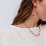 thin large octagon brass hoop earrings on model with brass link necklace and white shirt